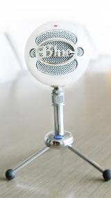 White Snowball brand microphone perches like a large snowball on top of a small chrome microphone stand.