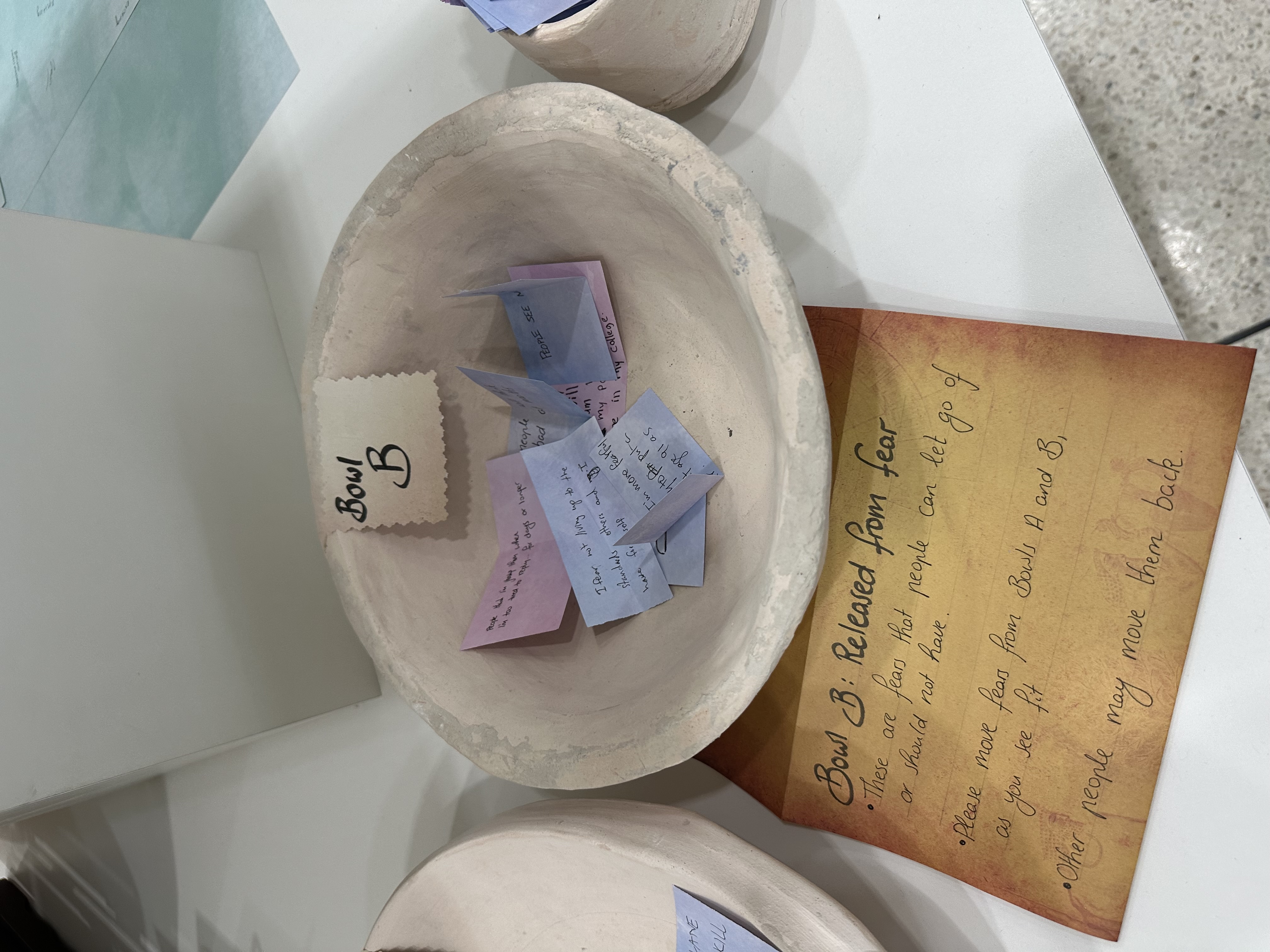 Clay, handmade bowl on a shelf, underneath is a paper reading "Bowl B: Release from Fear"