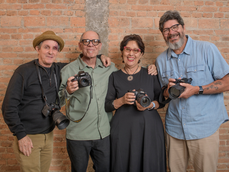 Four people posed with cameras in front of a brick wall
