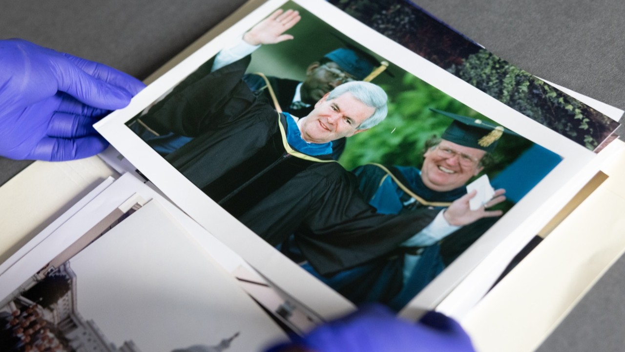 Gloved hands hold a photo of Newt Gingrich
