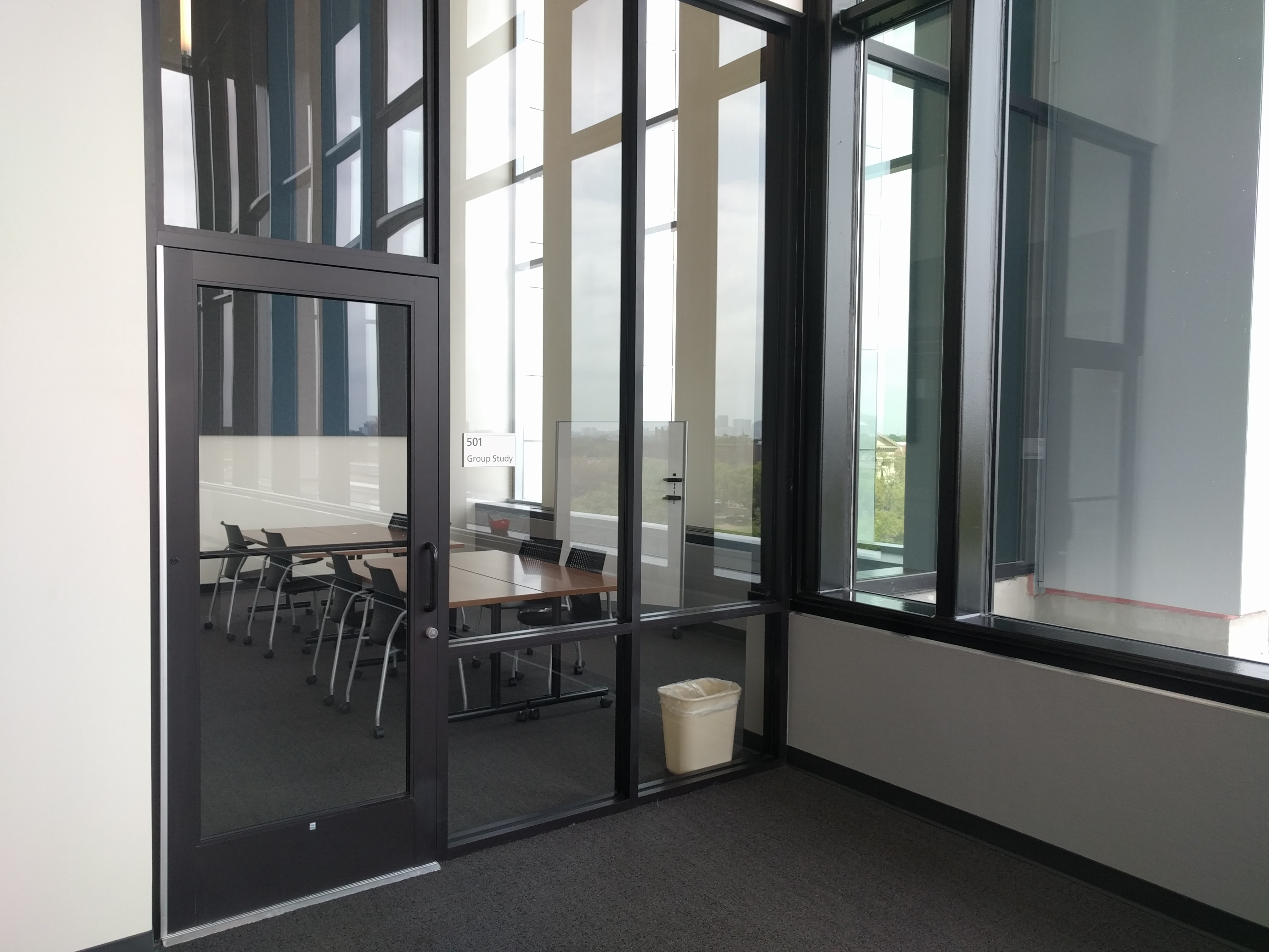 Fifth Floor Group Study Room shown behind its glass wall with tables and chairs for eight people.