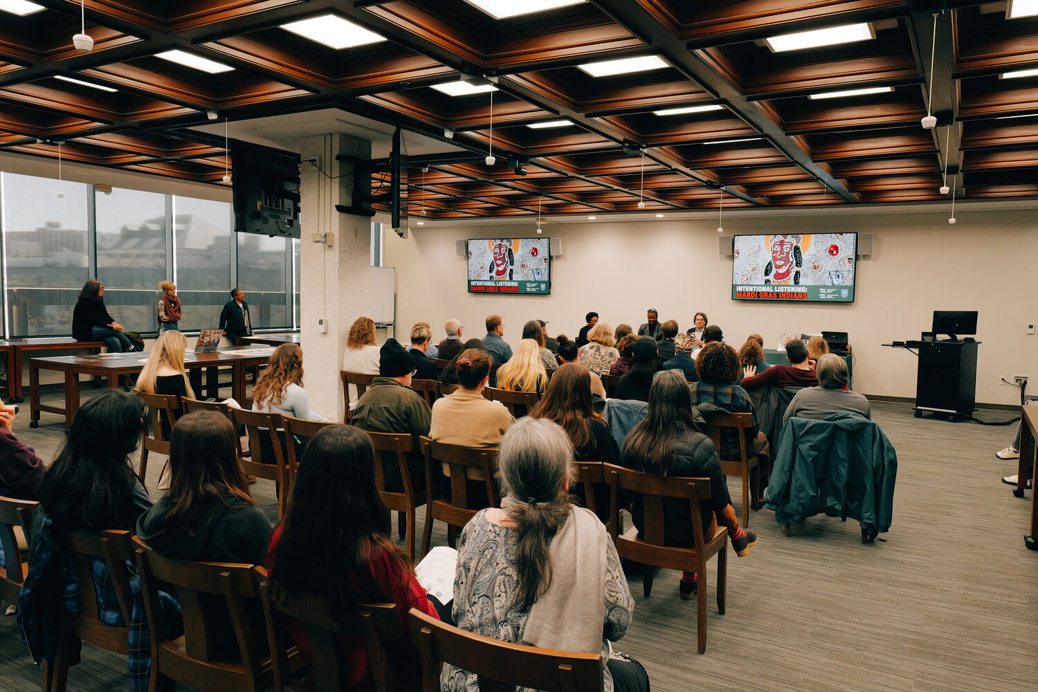 Guest sit in chairs looking at the three speakers.