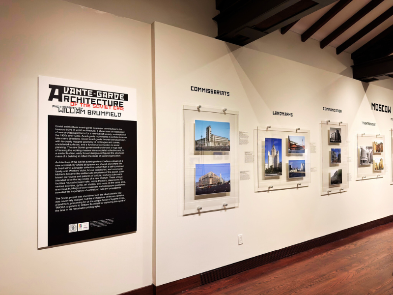 Photo of the exhibit - interior of gallery with large photos on wall of a russian buildings on the right is an information panel about the exhibit