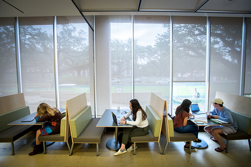 Students working along and in small groups at booth seating by the windows in the Learning Commons.