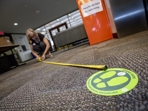 Dorothy Mackendrick prepares the library for social distancing protocols by measuring how far users should stand from the elevator.