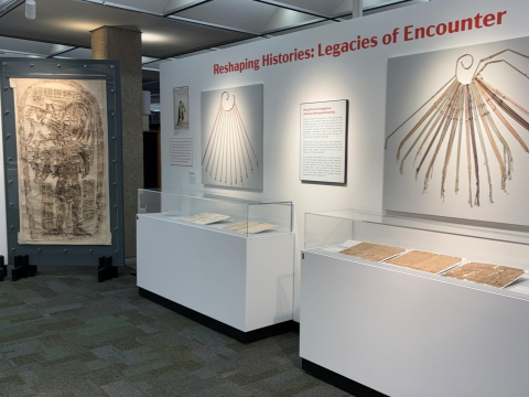 Photo of an exhibit in a library. on the wall in red reads "Reshaping Histories: Legacies of Encounters"