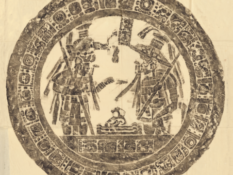 a circular rubbing of dark gray pigment on a light background depicting two individuals standing before a set of bones surrounded by an enscription in Maya script